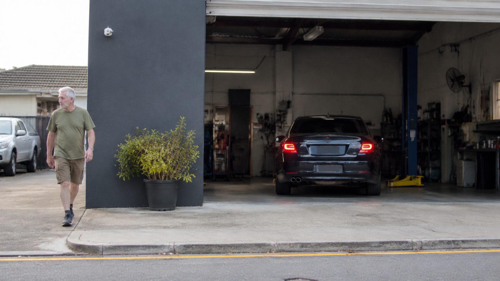 Car being reversed into a workshop bay with the owner walking back towards the street